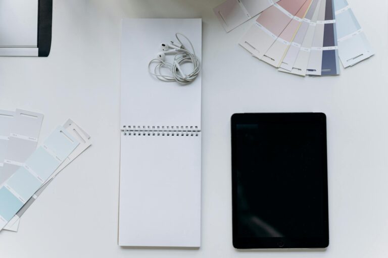 Top view of a flat lay with earphones, notepad, tablet, and color swatches for design inspiration.